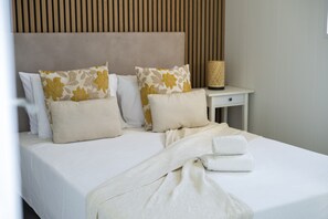 A neatly made bed with floral pillows, a bedside table with a lamp, and a headboard with vertical slats.