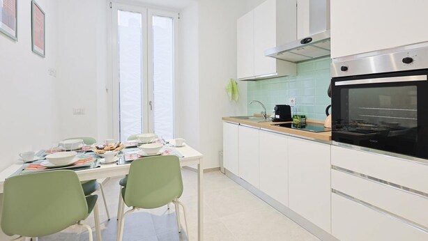Een moderne keuken met witte kastjes, een zwarte oven en een raam met zonwering.