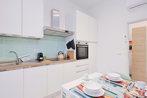 A modern kitchen with white cabinets, a stainless steel range hood, a built-in oven, and a wooden countertop.