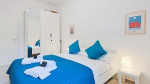Een hotelkamer met een bed, een kledingkast, een nachtkastje met een lamp, en twee ingelijste foto's aan de muur.