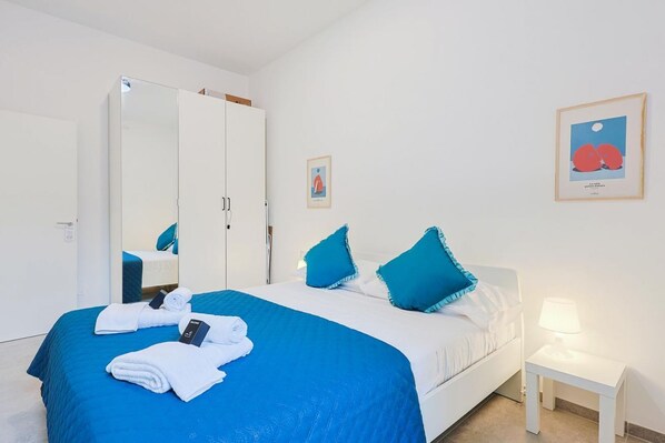 A hotel room with a bed, a wardrobe, a bedside table with a lamp, and two framed pictures on the wall.