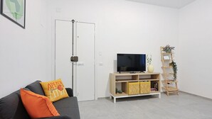Een woonkamer met een bank, een televisie, een houten tv-meubel, een deur en een plantenplank.