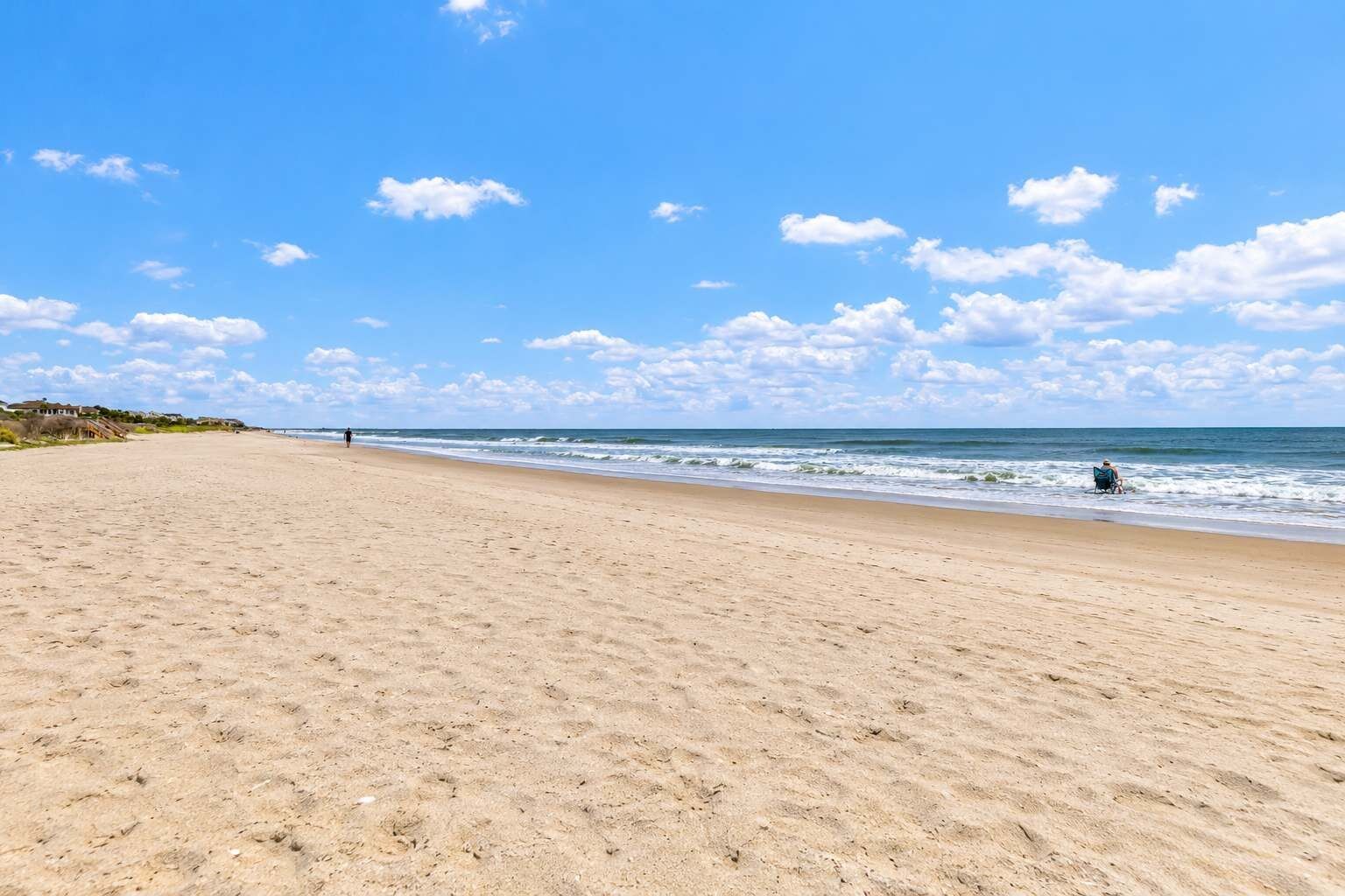 A wide sandy beach with a clear sky and a few clouds.