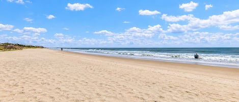 A wide sandy beach with a clear sky and a few clouds.