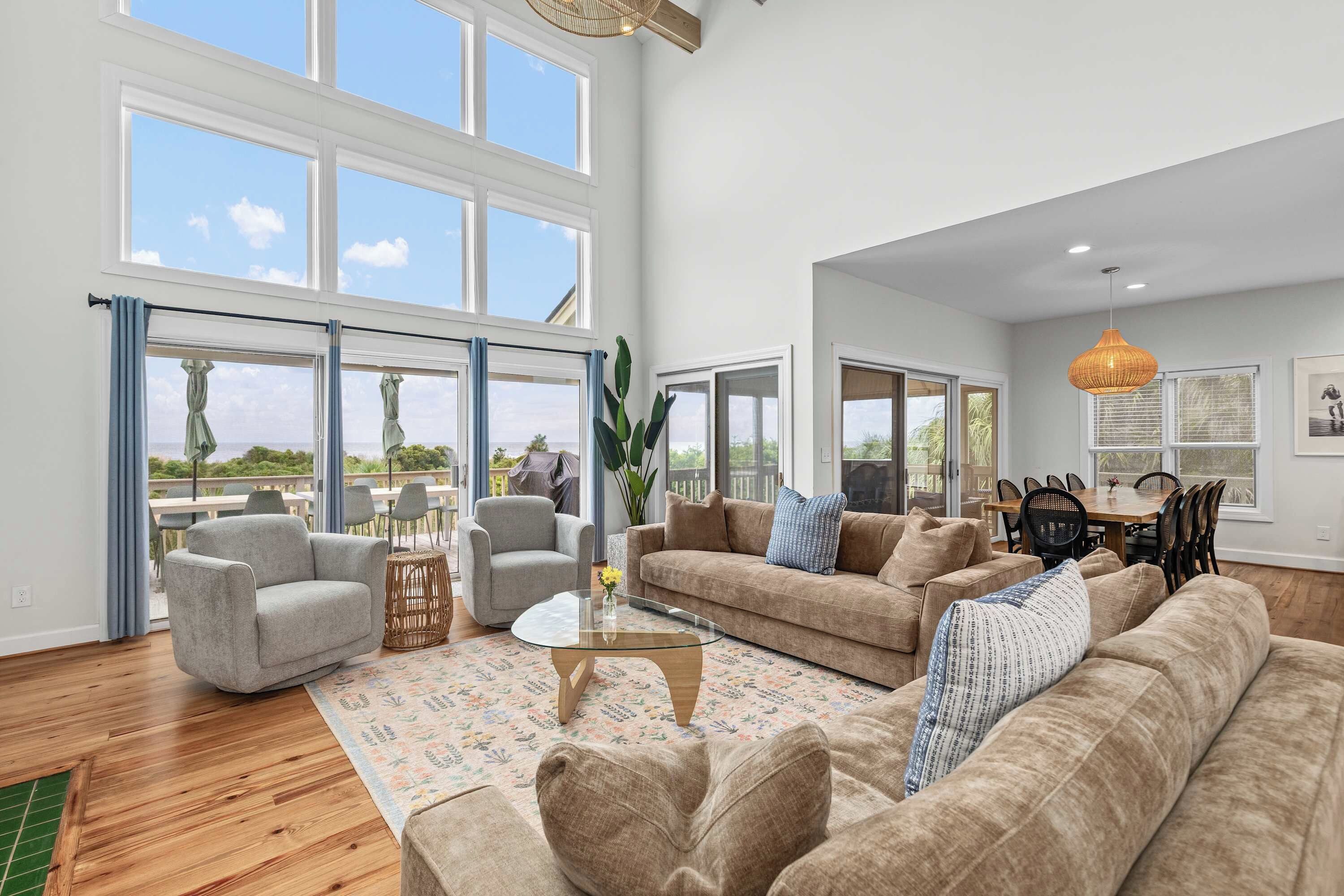 A spacious living room with large windows, a dining area, and a kitchen.