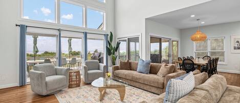 A spacious living room with large windows, a dining area, and a kitchen.