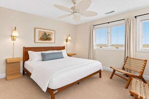 Ein Schlafzimmer mit einem Bett, zwei Nachttischlampen, einem Deckenventilator, einem Fenster mit Vorhängen und einem Korbstuhl.