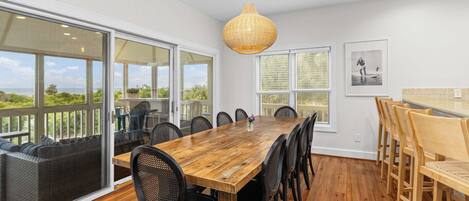 Un amplio comedor con una gran mesa de madera, sillas negras y una lámpara colgante de mimbre.
