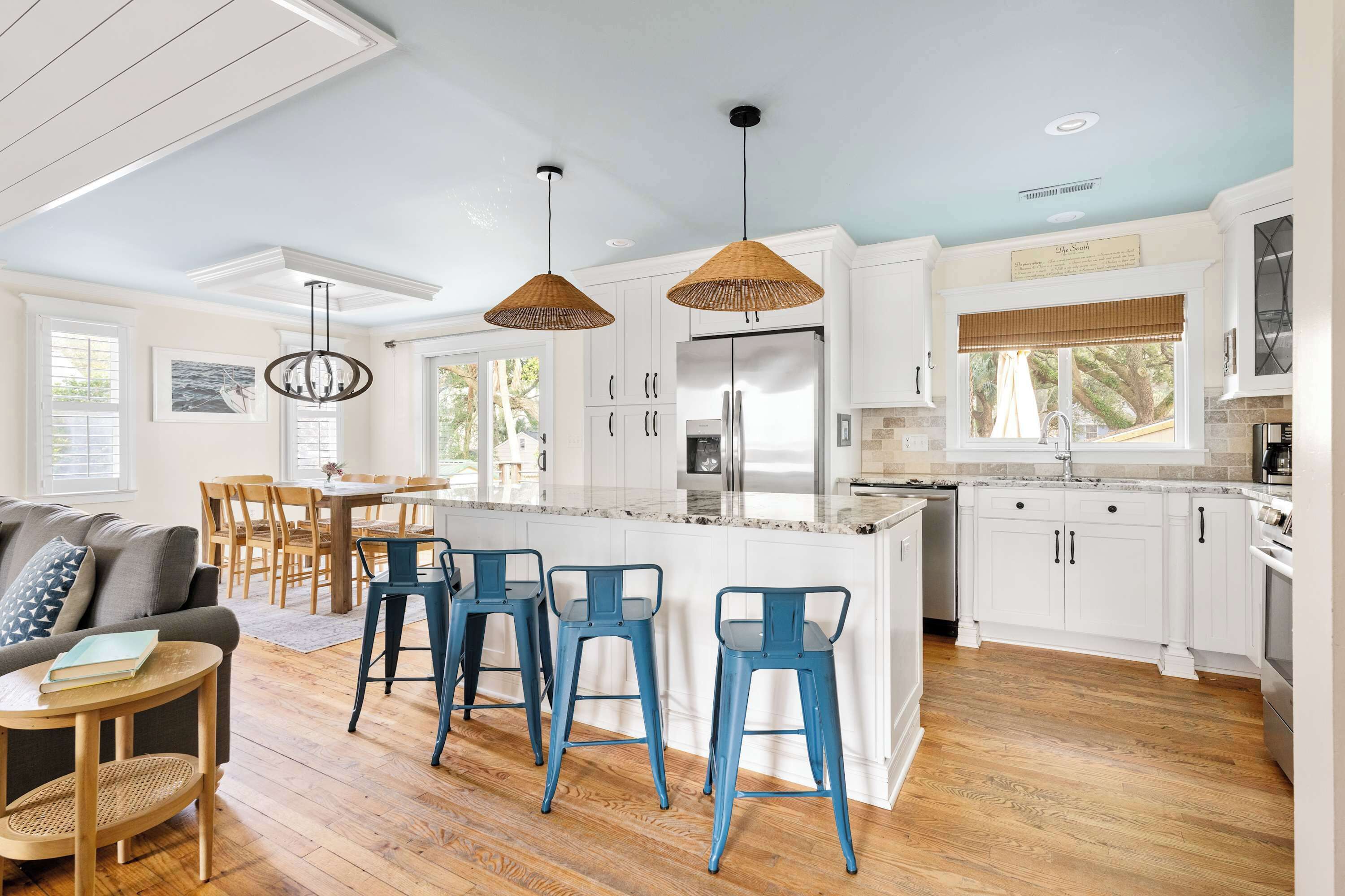 A modern kitchen with white cabinets, a central island, blue bar stools, and pendant lighting.