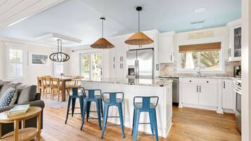 A modern kitchen with white cabinets, a central island, blue bar stools, and pendant lighting.