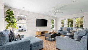 A modern living room with a grey sofa set, a flat-screen TV mounted on the wall, and a ceiling fan.