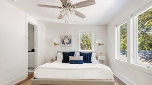 A bedroom with a bed, a ceiling fan, a window, and a wall-mounted artwork.
