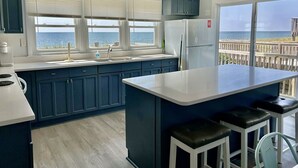 A kitchen with a large island, a view of the ocean, and a balcony with a wooden railing. - Experience oceanfront luxury at A Waters Edge Escape in Oak Island, NC. (Oak Island)