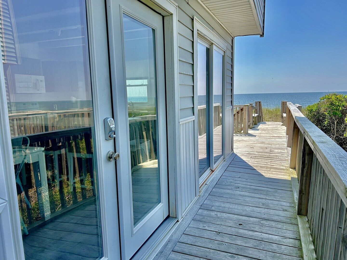 A wooden deck with glass doors leading to a balcony overlooking the ocean.
