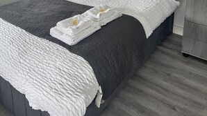Ein modernes Schlafzimmer mit einem großen Bett, grau-weißer Bettwäsche, einem Nachttisch mit Lampe und einem Fenster mit Ausblick.