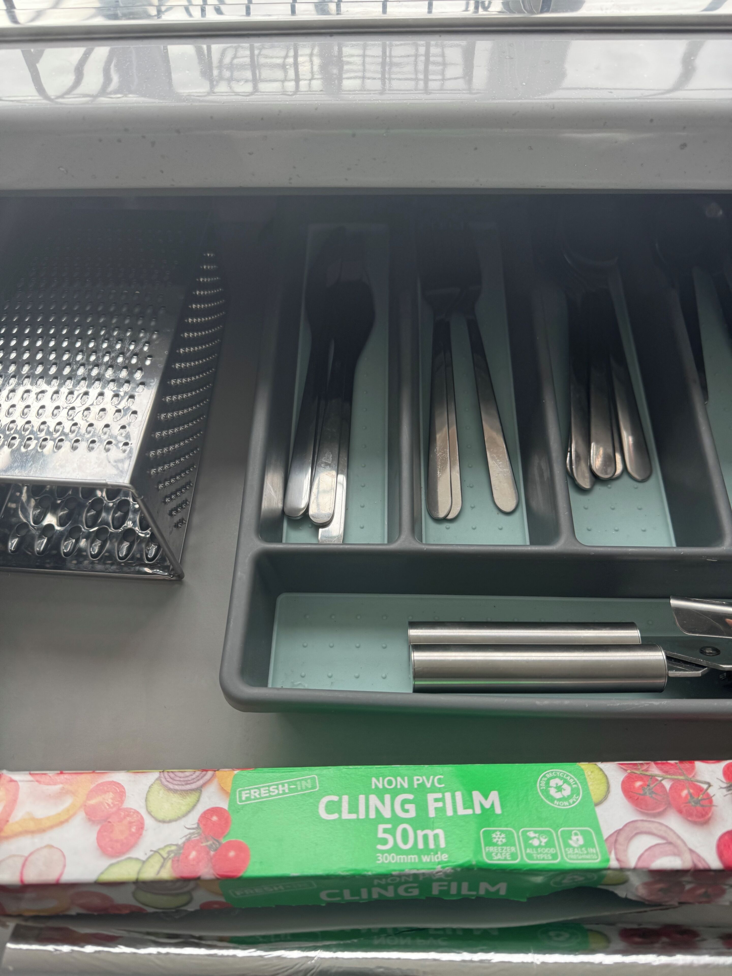 Un compartimento con un rallador, cuchillos y una caja de film transparente.