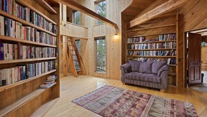 A spacious room with wooden bookshelves, a purple sofa, and a patterned rug. - Poplar 35 - Fun 3 Level Home, Pool Table, A/C, Hot Tub (Sunriver)