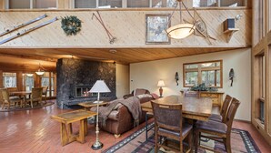 A spacious living area with a stone fireplace, wooden furniture, and a large dining table. - Poplar 35 - Fun 3 Level Home, Pool Table, A/C, Hot Tub (Sunriver)