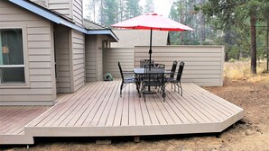 A wooden deck with a table and chairs, a red umbrella, and a house in the background. - Poplar 32 - Rec Passes for SHARC, Updated home, Centrally located, Private Hot Tub (Sunriver)
