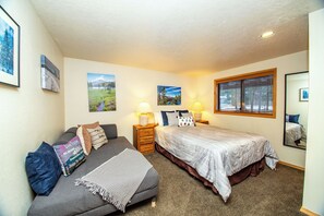A bedroom with a bed, a sofa, two bedside tables with lamps, and framed pictures on the walls.