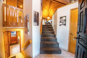 Una escalera con peldaños alfombrados que sube a un segundo piso, una puerta de madera con manija de latón y un letrero de bienvenida con silueta de árbol.