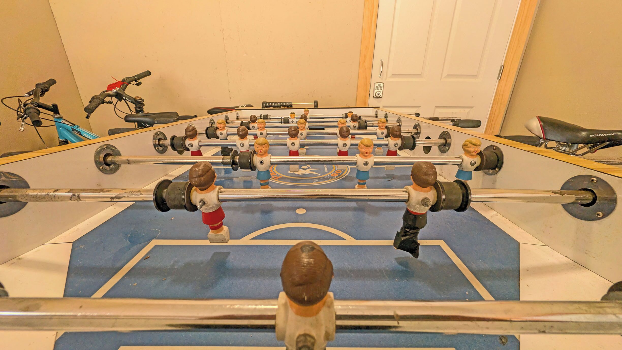 A foosball table in a room with a door, a bicycle, and a scooter.