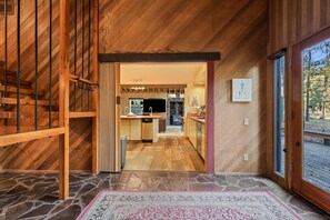 A wooden interior with a stone floor, a kitchen with a stone stove, and a view through a glass door.