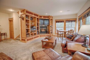 A cozy living room with a fireplace, wooden shelves, a leather sofa, and a dining area.