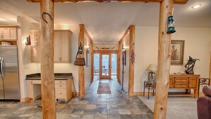 A spacious hallway with a stone floor, wooden beams, and a view into a dining area with a table and chairs. - Red Fir 14 - Outdoor Living, Steps to Village & SHARC, Passes included (Sunriver)