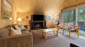 Interior acogedor de una cabaña de madera con chimenea, un sofá, una mesa de centro de madera y dos sillones de mimbre.