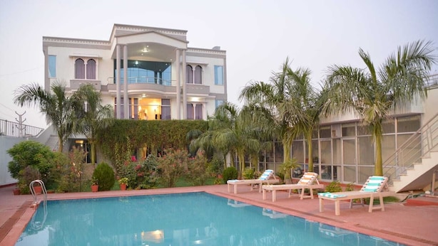 Un área de piscina con sillones de descanso y un edificio grande con múltiples ventanas y balcones.