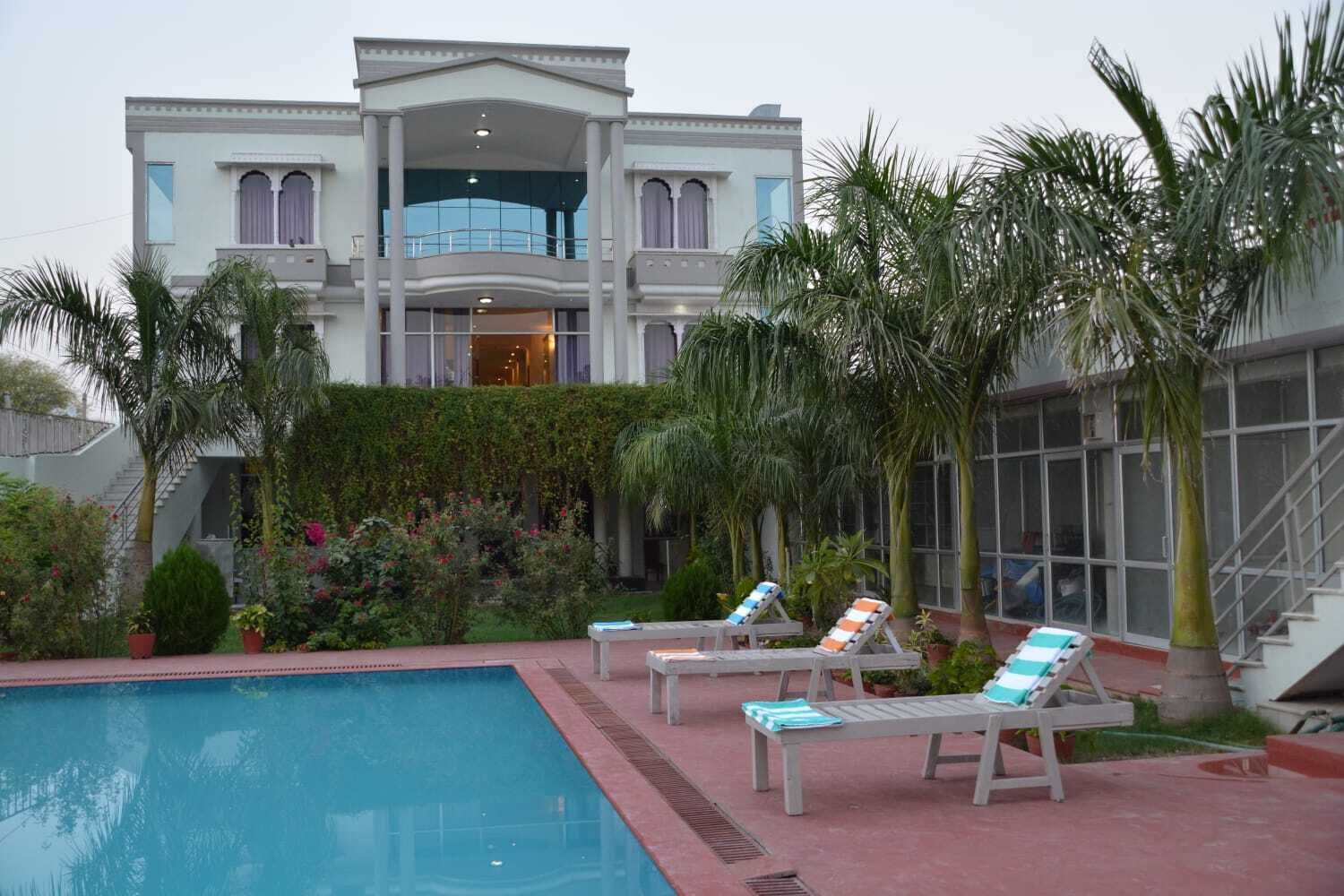 A large, two-story building with a swimming pool, palm trees, and lounge chairs.