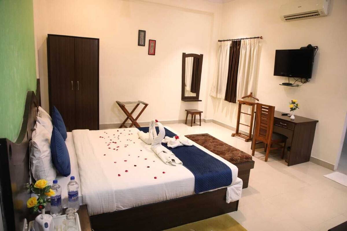 A hotel room with a bed, a desk, a chair, a wardrobe, and a television.
