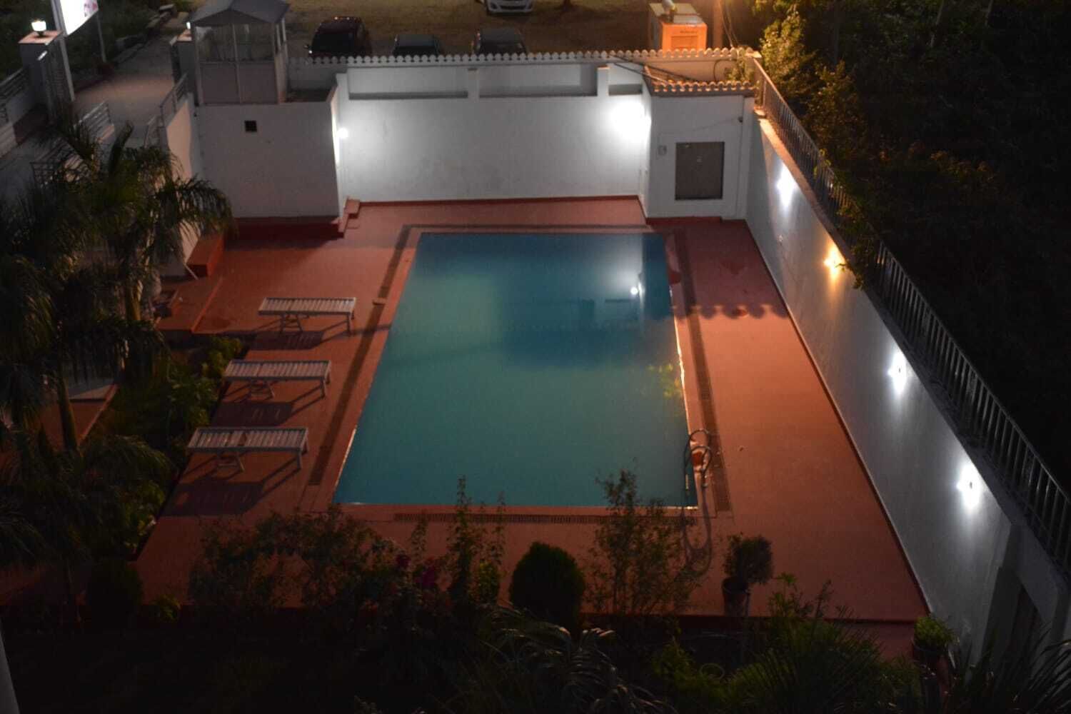 A rectangular swimming pool with a tiled deck, surrounded by a low white wall and a metal fence.