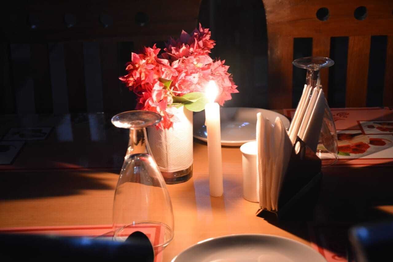 Une table avec une bougie, un vase de fleurs, un verre et un menu.