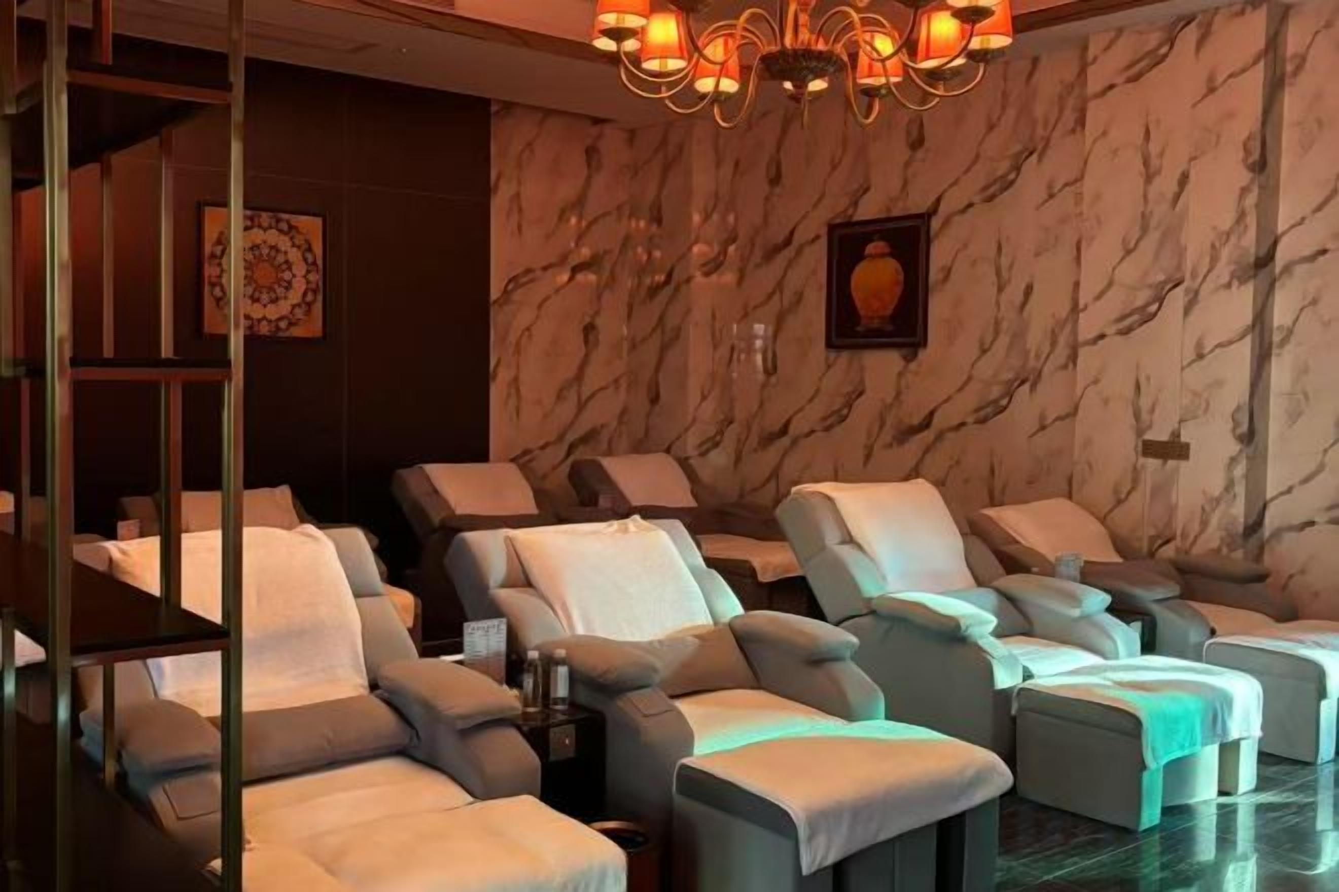 A massage room with multiple massage chairs, a marble wall, and a chandelier.