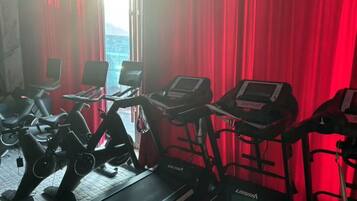 A gym with stationary bikes and treadmills, red curtains, and a view of a cityscape.