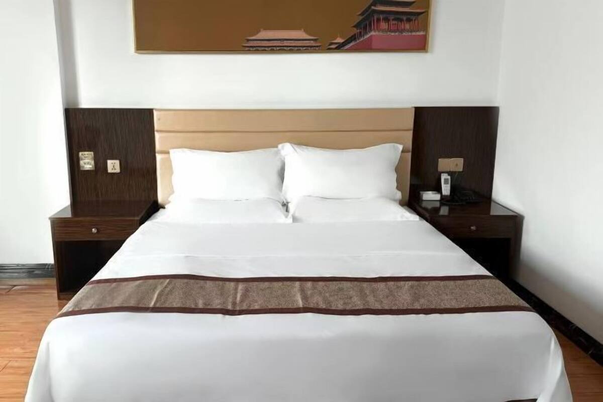 A hotel room with a large bed, two nightstands, a wall-mounted painting, and a wooden floor.