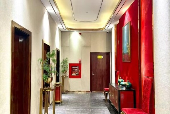 A hotel hallway with a red wall, a wooden door, a reception desk, and a plant. - Meihao Hotel (Sihanoukville)