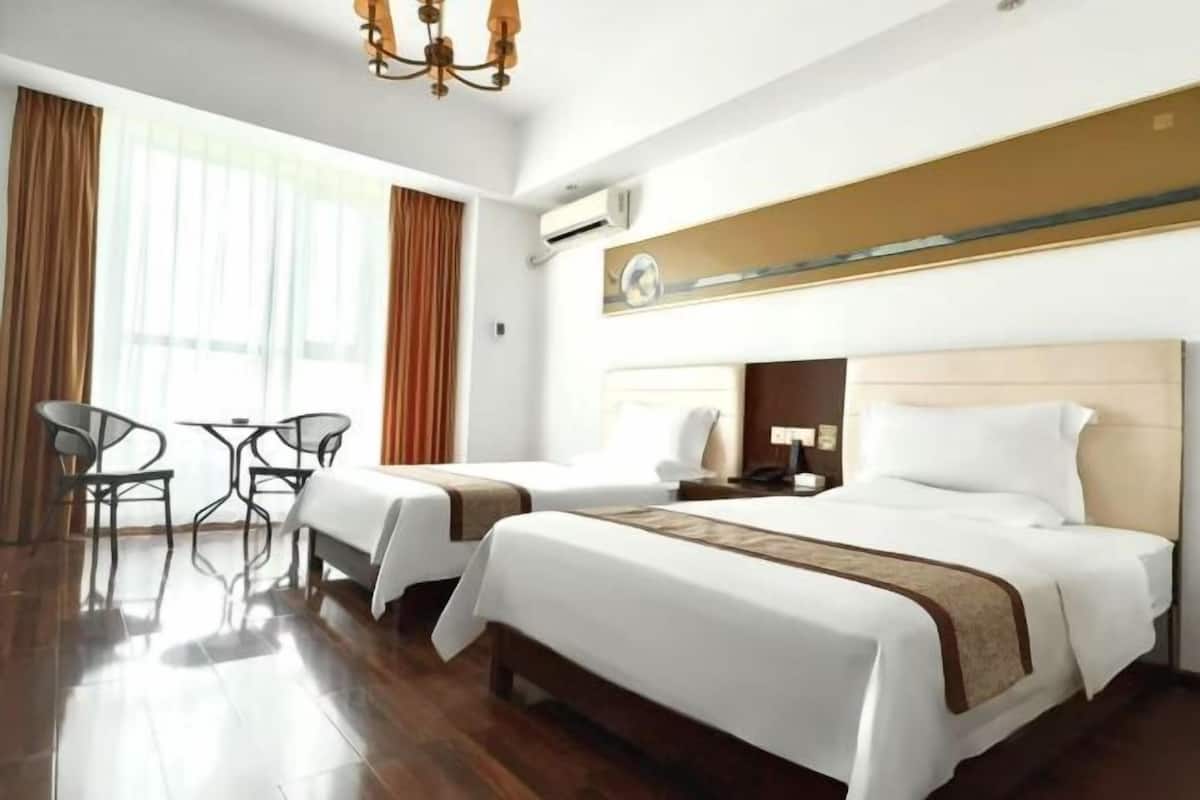 A hotel room with two beds, a dining area with chairs, a chandelier, and a large window with curtains.