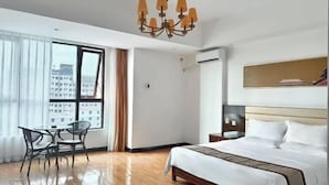 Un cuarto de hotel con una cama grande, un candelabro, una mesa de comedor con sillas y vistas a la ciudad por la ventana.