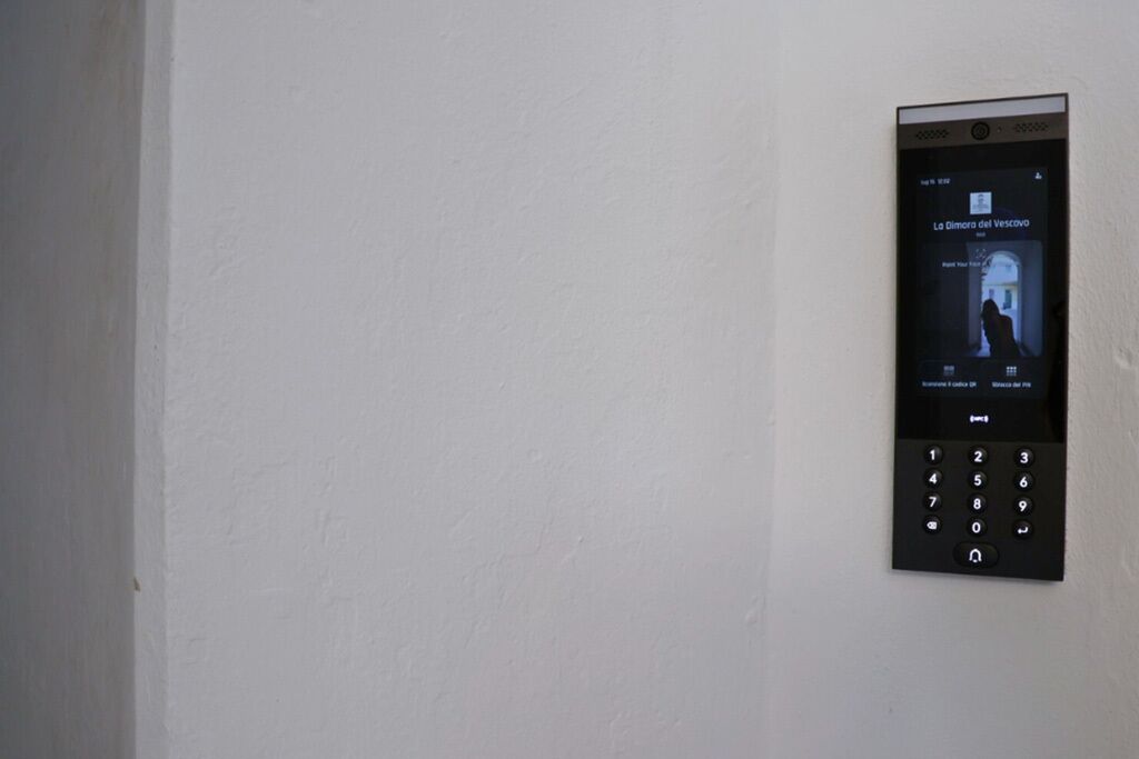 A wall-mounted electronic device with a screen displaying a video titled "La Gimarra del Vescovo."