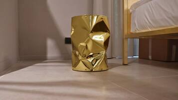 A modern room with a unique gold-colored cylindrical object on the floor, a bed with white bedding, and a plain wall.