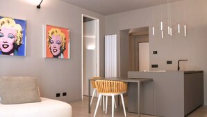 Un salon moderne avec un canapé, un coin repas comprenant une table et des chaises, un espace cuisine avec un comptoir, et des œuvres d’art accrochées aux murs.
