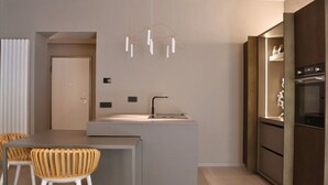 Une cuisine moderne dotée d’un îlot central, d’un four encastré et d’un luminaire suspendu.