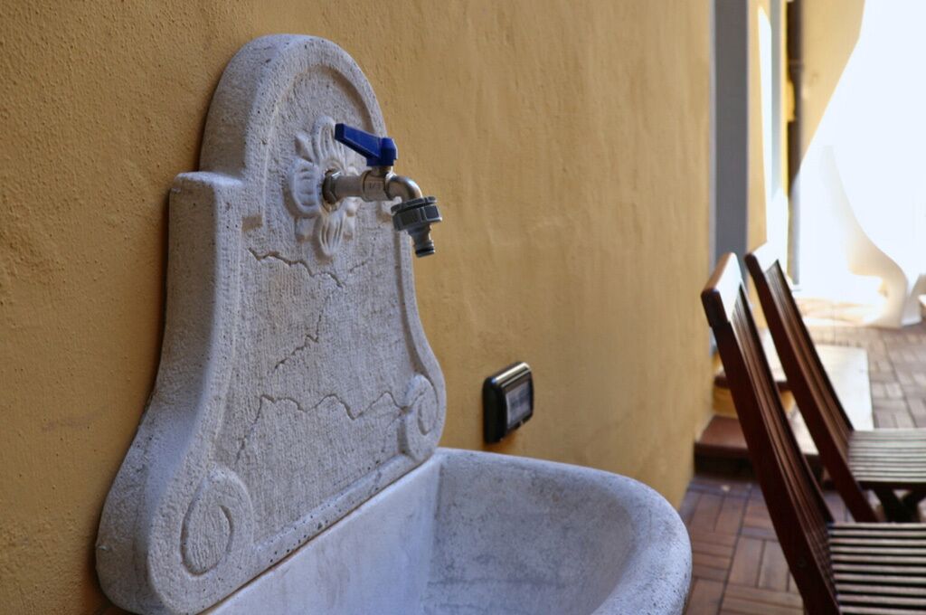 Een stenen wastafel met een kraan en een schakelaar bevestigd aan de muur, waarschijnlijk in een openbaar toilet.