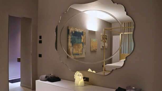 Une salle de bain moderne avec un grand miroir, un meuble-lavabo blanc et un escalier visible dans le reflet.