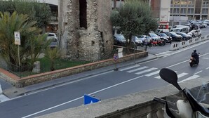 Une rue bordée d’une tour de pierre historique, de scooters garés et d’un bâtiment sur lequel on peut lire l’inscription « BAR ».
