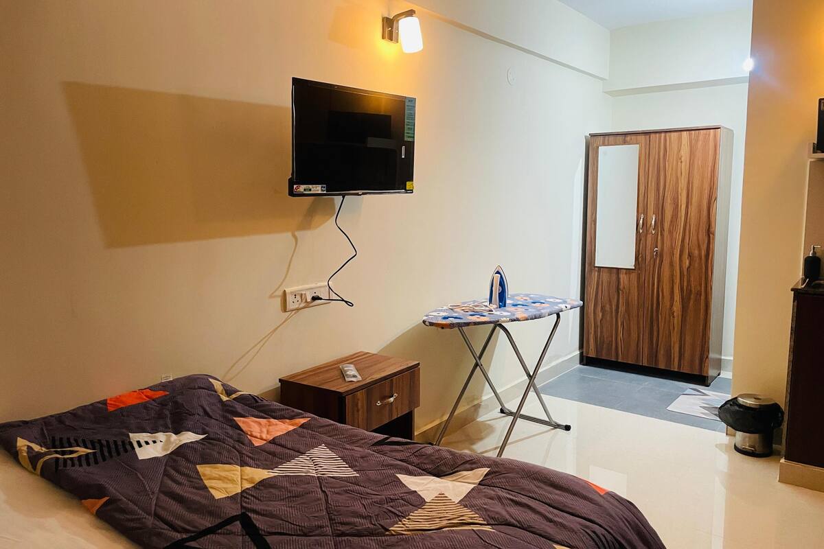 Une chambre d’hôtel comprenant un lit, un téléviseur fixé au mur, une petite table avec un fer à repasser et une planche à repasser, et une armoire en bois.