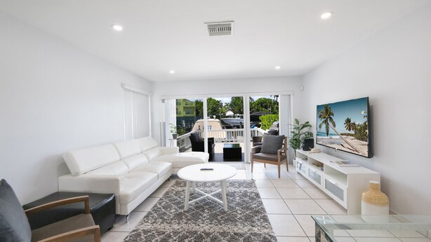A modern living room with a white sofa, a round coffee table, and a TV on the wall. - Intracostal Beauty in Fort Lauderdale (Fort Lauderdale)